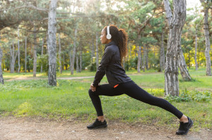 Tips for Running - Image of sportswoman 20s wearing black tracksuit working out, and stretching body in green park
